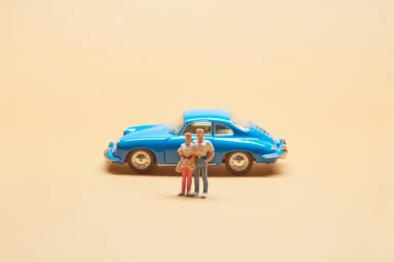 A miniature family standing in front of a classic blue toy car on a beige background, representing family travel concepts.
