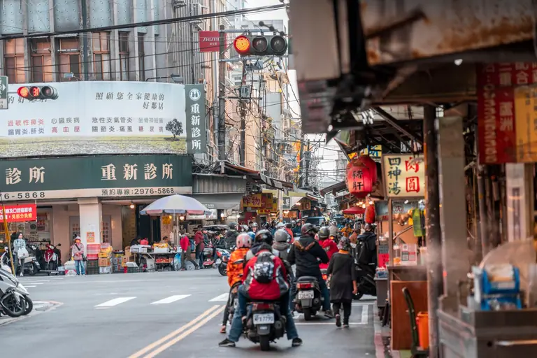 Vibrant Asian city street crowded with motor scooters, traffic, and urban life.