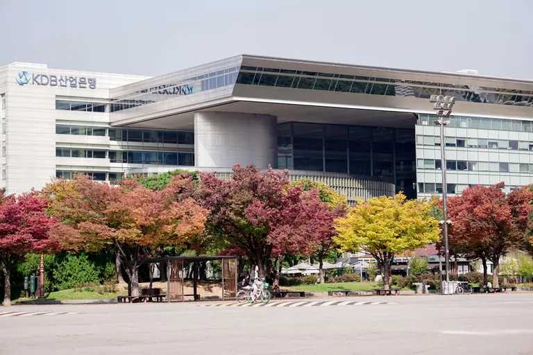 A modern urban building surrounded by colorful autumn trees in a cityscape setting.