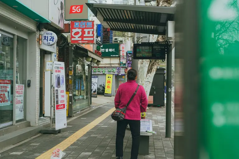 A person waits at a bus stop in Seoul, South Korea, featuring vibrant street signage.