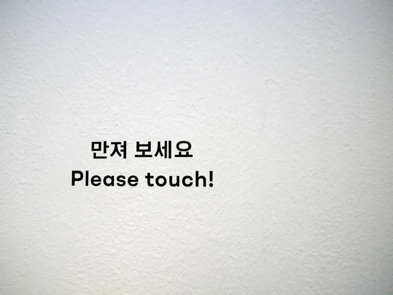 a white wall with a sign that says please touch