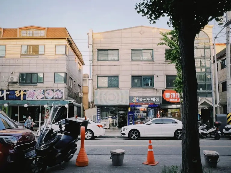 Bustling street view in Ansan-si, South Korea, featuring traffic, shops, and buildings on a sunny day.