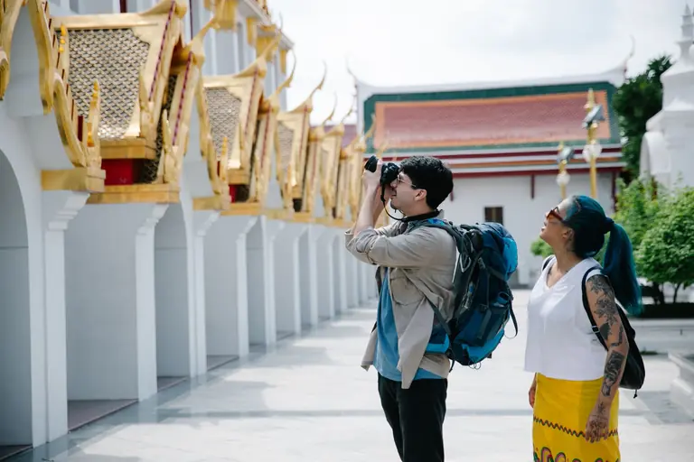 A couple with backpacks photographing a temple during daylight visit.