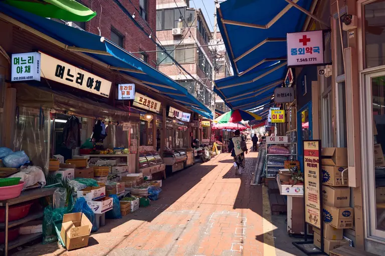 Bustling outdoor market in Seoul with colorful stalls under blue awnings.