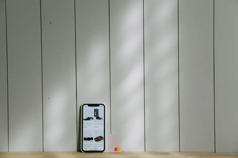 A smartphone and credit card sit on a wooden surface with soft lighting shadows.