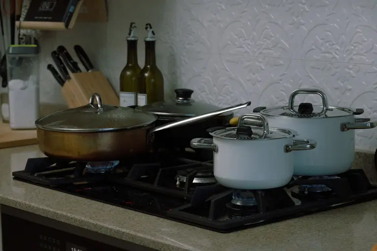 A home kitchen scene featuring pots and pans on a gas stove, showcasing a warm cooking setting.
