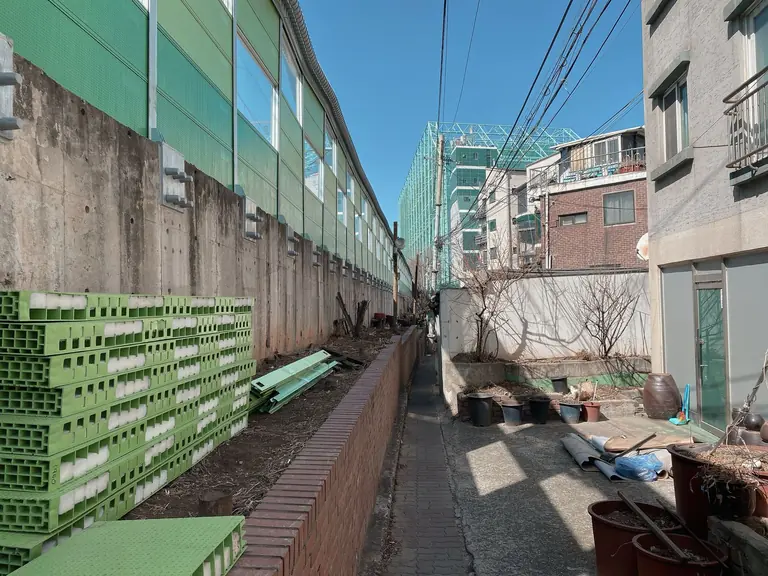 Explore a narrow urban alleyway in Seoul, surrounded by buildings and vibrant green accents.