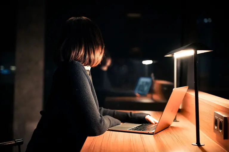 A woman works on her laptop under warm lighting, creating a calm nighttime atmosphere.