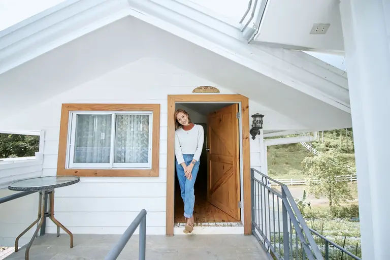 Woman smiling at a lovely cabin entrance, showcasing a peaceful outdoor setting.