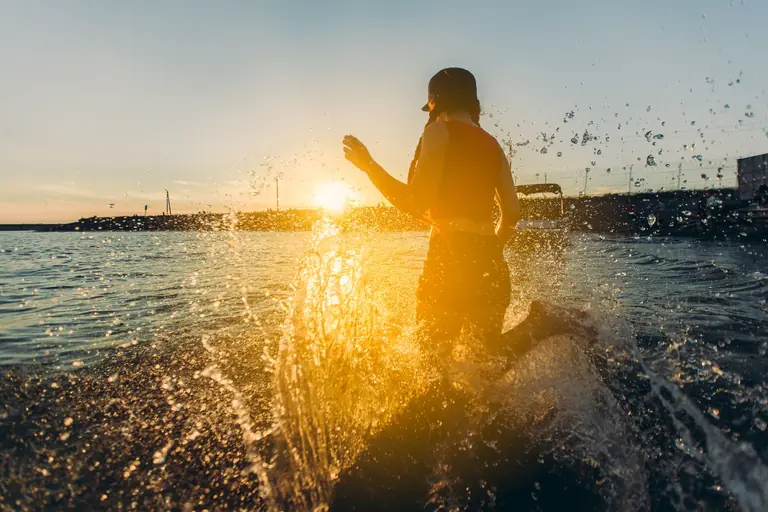 A silhouette of a person enjoying the ocean waves during a vibrant sunset.