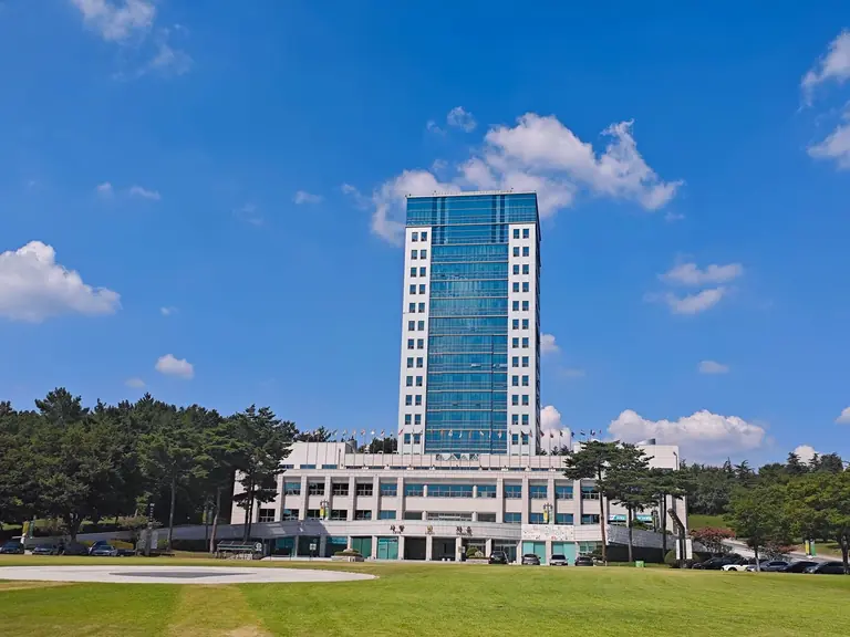 Tall office building under clear blue sky, surrounded by trees and grass lawn.