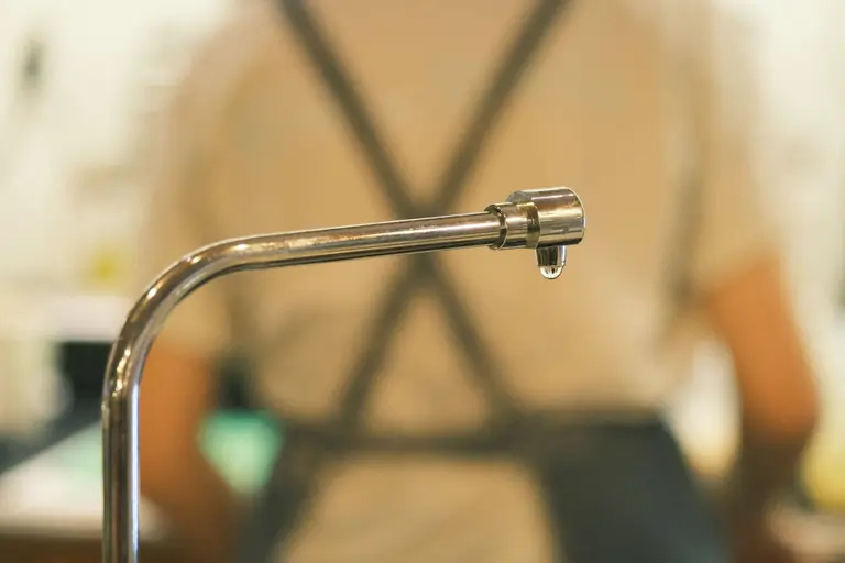 A focused shot of a metal faucet with a single drip indoors, capturing water conservation.