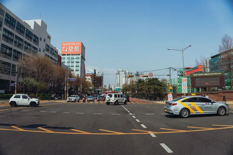 Street view of a busy intersection in Seoul, South Korea with cars and pedestrians.
