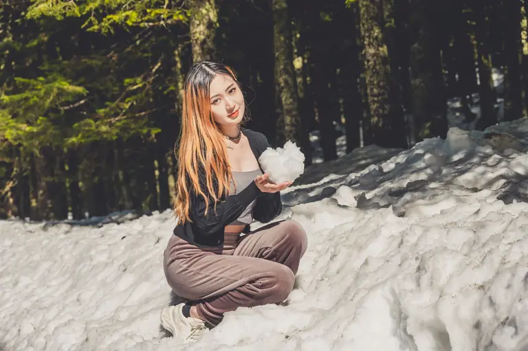 Asian woman holding snow in a forest during winter season.