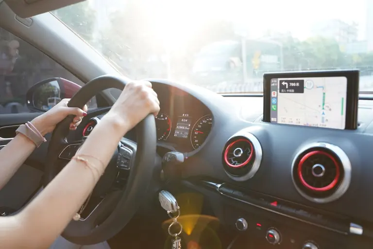 Hands on steering wheel using GPS navigation inside car during road trip.