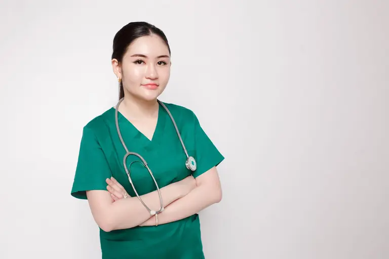 Portrait of a confident nurse in green scrubs with crossed arms and stethoscope, indoor studio setting.