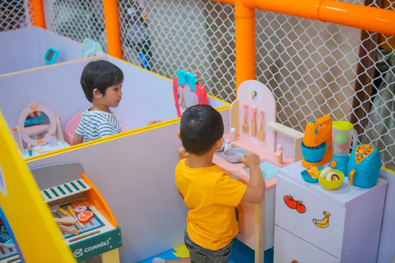 Two kids playing with kitchen toys in a colorful indoor play area.