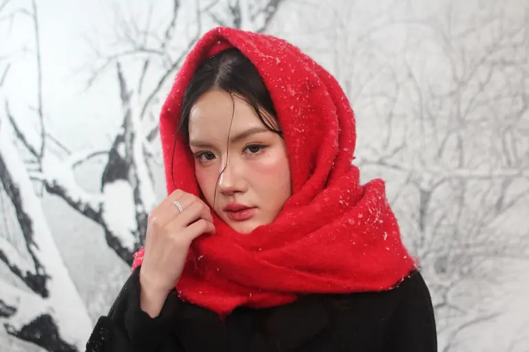 A woman wearing a red scarf stands in snowfall, creating a vibrant winter portrait.