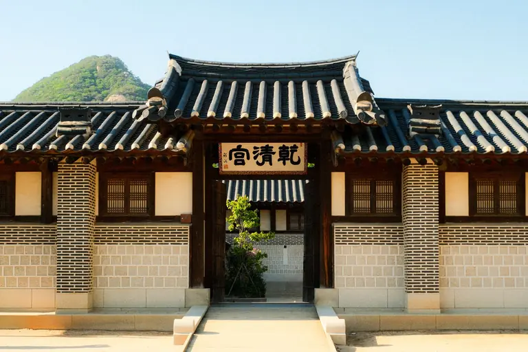 A scenic view of a traditional Korean building with a mountain backdrop under a clear blue sky.