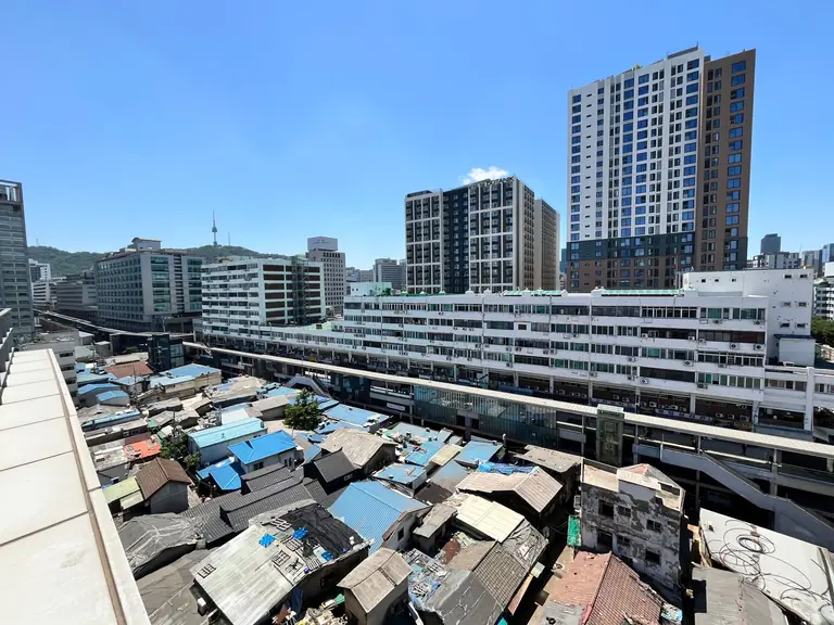 An urban area with modern high-rise buildings and older rooftops under a clear blue sky.